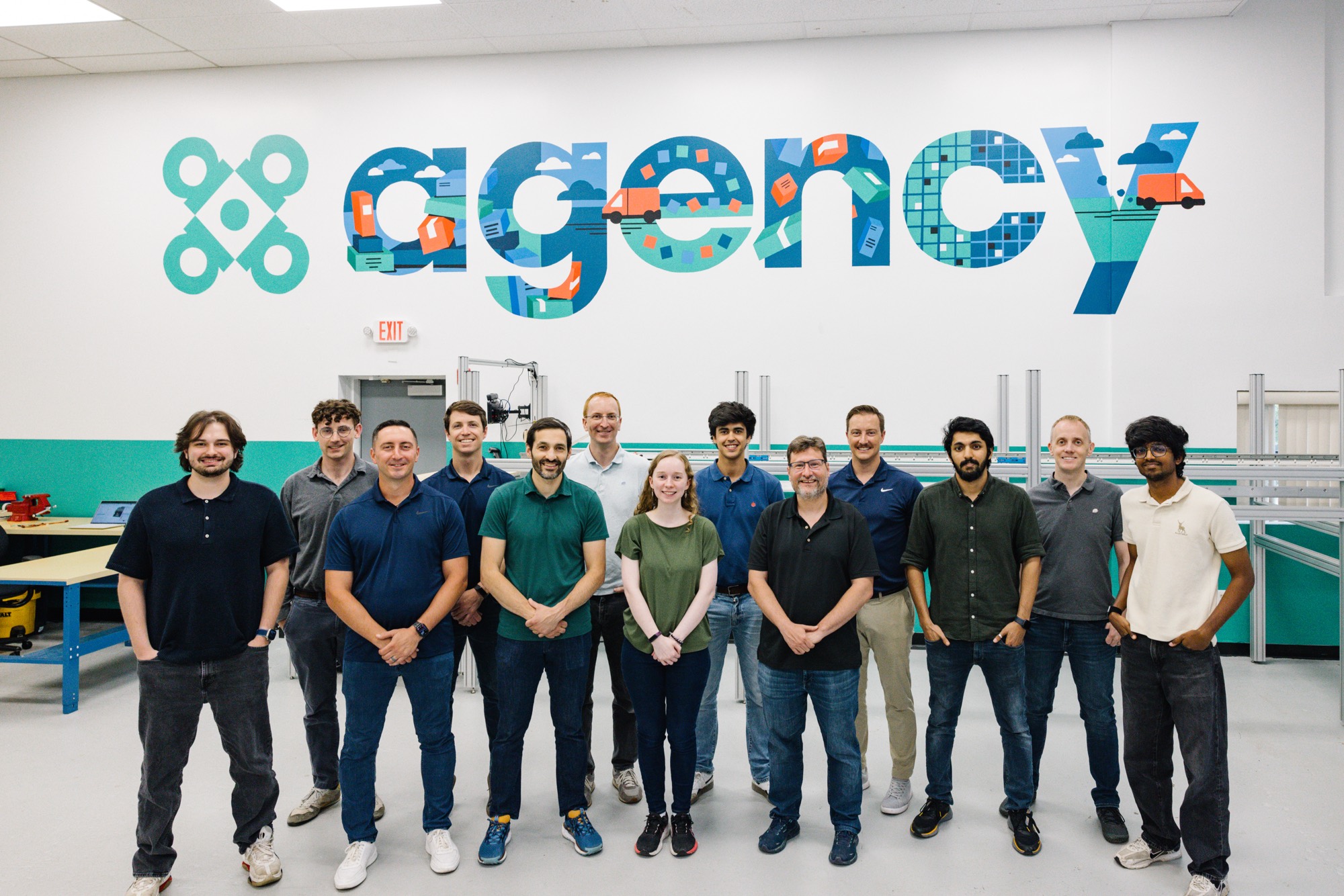 The Agency Robotics team together in front of the agency mural at the Woburn workshop